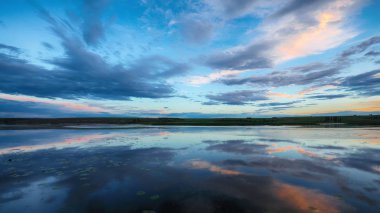 Göl üzerinde dramatik gün batımı. Nilüferler göl kenarında. Göl kenarında gökyüzü ve bulutlar yansıma