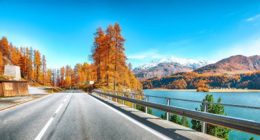 Sils Gölü 'ndeki (Silsersee) fantastik sonbahar sahnesi ve sahildeki asfalt yol. İsviçre Alpleri 'nin renkli sonbahar sahnesi. Konum: Maloya, Engadine bölgesi, Grisons kantonu, İsviçre, Avrupa.