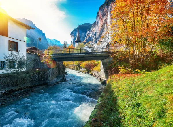 Amazing autumn landscape of touristic alpine village Lauterbrunnen with famous church and Staubbach waterfall. Location: Lauterbrunnen village, Berner Oberland, Switzerland, Europe.