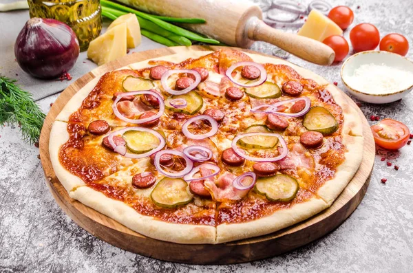 Homemade Meat Loves Pizza with pepperoni sausage, bacon, onions, cucumber, tomatoes, cheese on a wooden board, background, restaurant menu concept. Italian food style, close up.