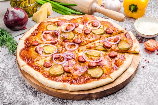 Meat Loves Pizza buatan sendiri dengan sosis pepperoni, bacon, bawang, mentimun, tomat, keju di papan kayu, latar belakang, konsep menu restoran. Italian food style, close up . Stok Gambar Bebas Royalti