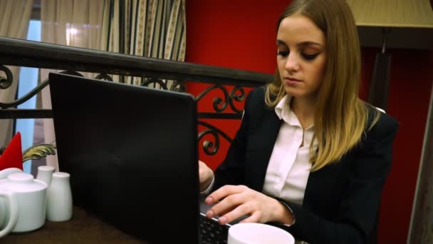 Een meisje in een pak in een café een tekst wordt afgedrukt achter haar eigen laptop — Stockvideo