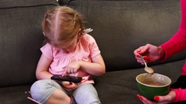 Annesi onu bir kaşık beslemeleri ise küçük bir kız onu smartphone vasıl görünüyor
