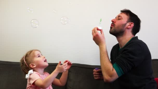 Een schattig klein meisje vangsten zeepbellen met haar vader in slow motion. — Stockvideo