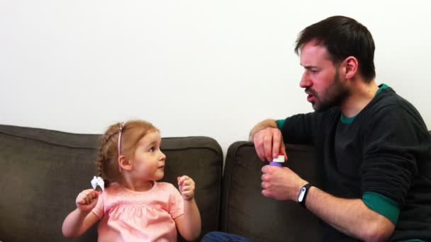 Una niña le muestra a su padre un tamaño de una burbuja de jabón que desea que sople — Vídeos de Stock