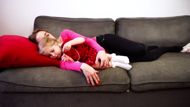 Uma mãe e uma pequena filha deitam-se no sofá e adormecem . — Vídeo de Stock