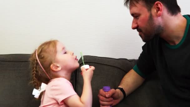 Una niña sopla burbujas de jabón y su padre las atrapa por la boca . — Vídeos de Stock
