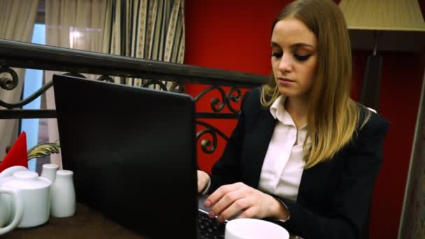 Young girl is typing on a laptop sitting in cafe — Stock Video