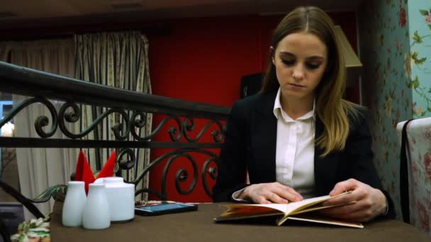 Una joven con chaqueta y blusa en un café para examinar el menú — Vídeo de stock