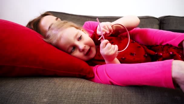 En flicka liggande på en soffa med mamman. — Stockvideo