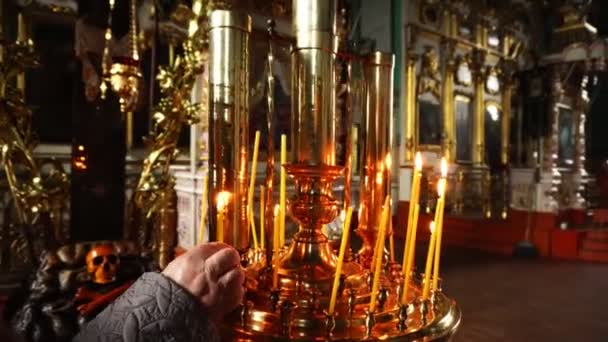 La mano humana pone una vela encendida en el templo . — Vídeos de Stock