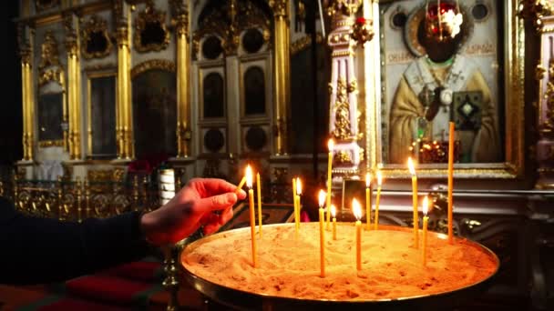 Een man in de kerk licht kaarsen die zijn gedoofd. — Stockvideo