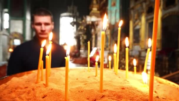 Aangestoken kaarsen op de voorgrond van het plan. Op de achtergrond is een man en een heleboel pictogrammen in de kerk. — Stockvideo