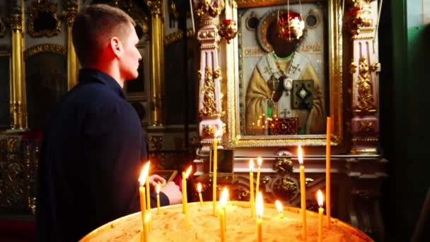 Людина молиться біля значка у храмі. На передньому плані плану запалюють свічки. — стокове відео