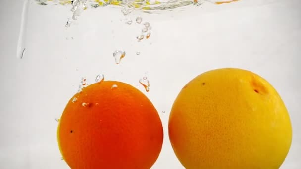 Un pomelo entero, naranja y limón cae al agua con burbujas. Video de cítricos en cámara lenta . — Vídeos de Stock