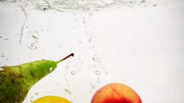 Ağır çekim meyve kabarcıkları ile. Bütün limon, elma ve armut şeffaf bir kaba su ile düşmek.