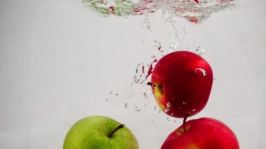 Ağır çekim video su kabarcıkları ile içine düşen kırmızı ve yeşil elma. Meyve izole beyaz zemin üzerine.