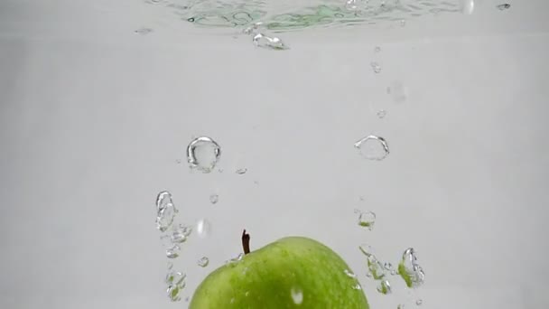 Une pomme verte tombe dans l'eau avec des bulles à un rythme lent. Pomme sur fond blanc isolé . — Video