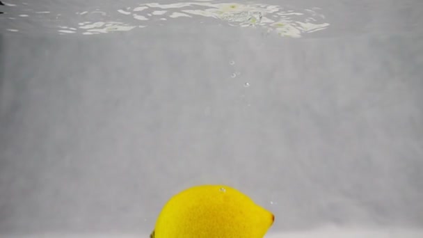 Un limón cae al agua con burbujas en cámara lenta. Frutos aislados sobre fondo blanco — Vídeos de Stock