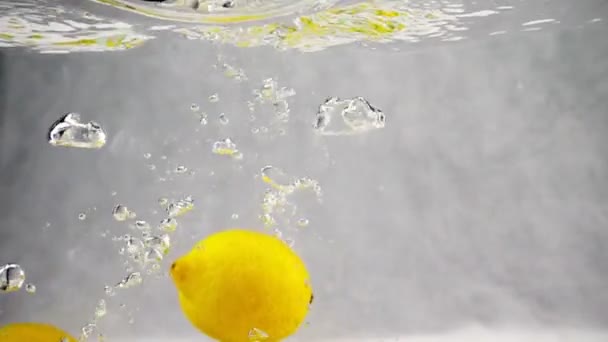 Желтые лимоны бросают в емкость с водой. Видео в замедленной съемке — стоковое видео