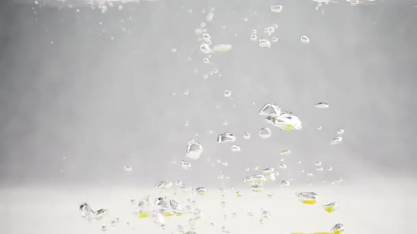 Citrons jaune vif tombant dans l'eau avec de grandes bulles au ralenti. Fruits sur fond blanc isolé . — Video