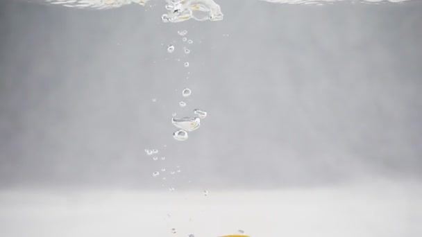 Orange tombant dans l'eau avec des bulles au ralenti. Fruits sur fond blanc isolé — Video