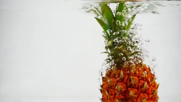 Спелый ананас падает в воду в замедленной съемке. Фрукты на белом фоне . — стоковое видео