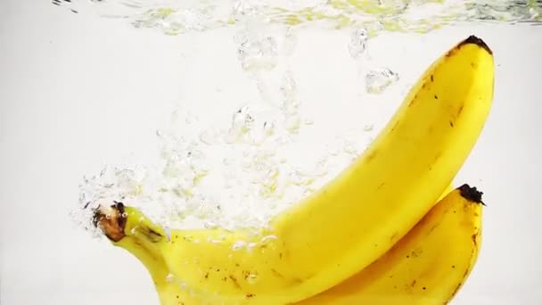 Die Bananen fallen mit vielen kleinen Blasen ins Wasser. Video von Bananen auf isoliertem weißen Hintergrund. — Stockvideo