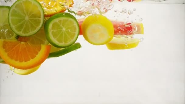 Куски цитрусового лайма, лимона, апельсина, грейпфрута падают в воду с брызгами и пузырьками, замедленное движение крупным планом — стоковое видео