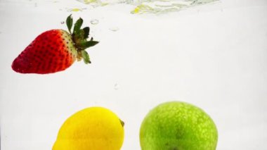 Çilek, limon ve elma suya düşer ve yavaş çekimde kabarcıklar oluşur..