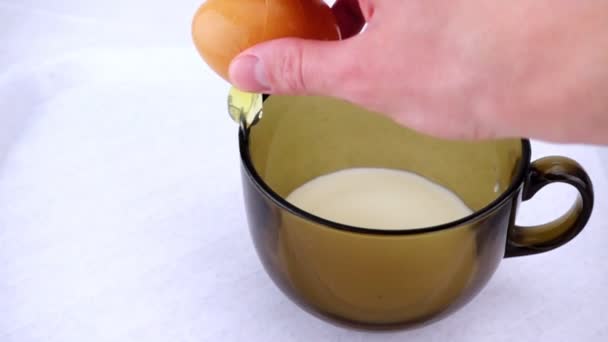 Человеческая рука медленно разбивает сырое яйцо в миску с молоком. — стоковое видео