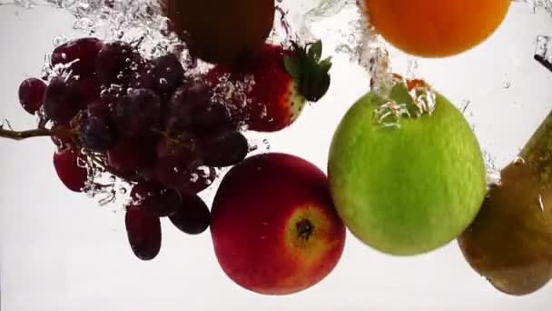 Äpple, kiwi, apelsin, päron, citron, druvor och jordgubbar faller i vatten med bubblor. Video i slow motion. — Stockvideo