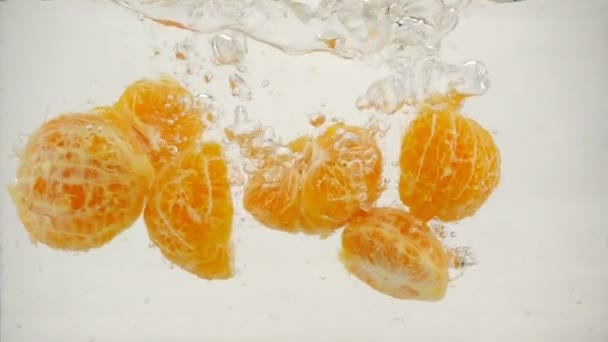 La mandarina de medio pelado cae en agua con burbujas, el movimiento lento se cierra. — Vídeos de Stock