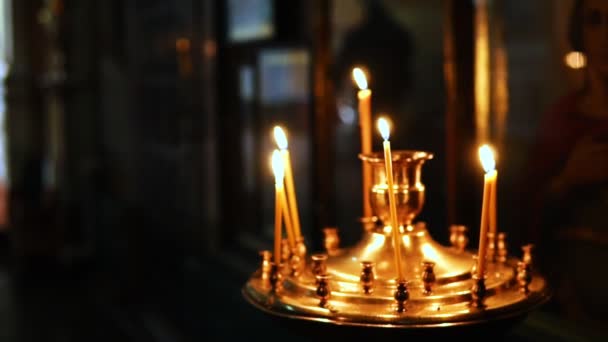 En person sätter ett ljus i en ljusstake framför religiösa ikoner — Stockvideo