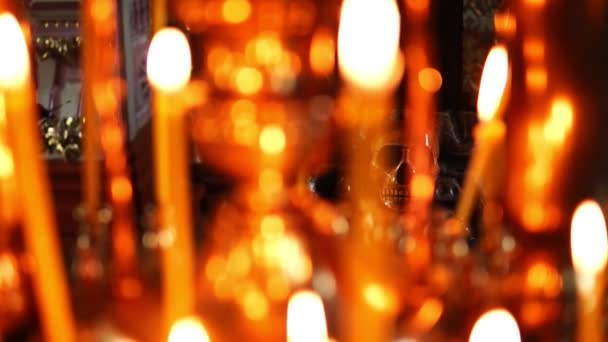 Calavera en foco, en primer plano encendiendo velas en la Iglesia Ortodoxa Cristiana — Vídeos de Stock