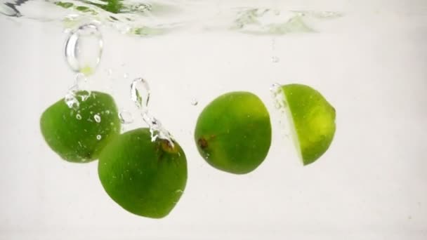 Metà succose di lime cadono in acqua con bolle e spray, poi cade il limone, primo piano al rallentatore — Video Stock