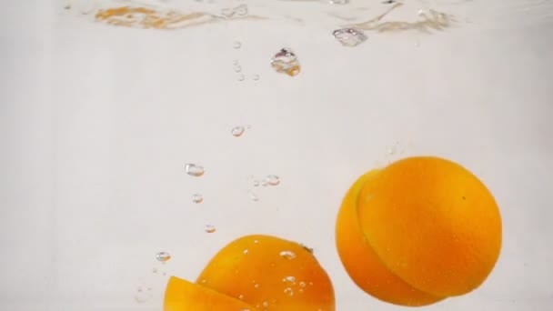 Отрезанные апельсины быстро погружаются в воду с пузырьками, замедленным движением крупным планом — стоковое видео
