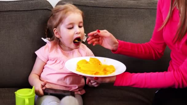 En liten flicka leker med sin smartphone medan hon matas frukt — Stockvideo