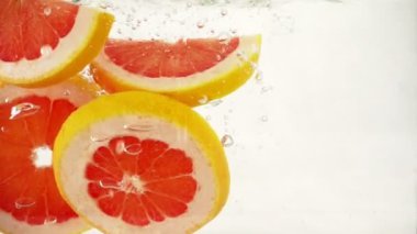 Su sıçramalarına ve kabarcıklar, ağır çekim yakın çekim ile greyfurt portakal dilimleri düşmek