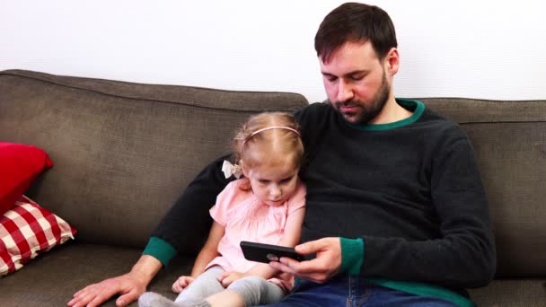 Far och dotter tittar på smartphone sitter i soffan — Stockvideo