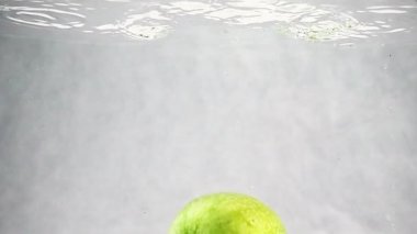 Yeşil elma yavaş bir hızda suya düşüyor. Beyaz bir arka plan üzerinde izole meyve.