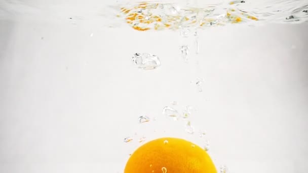 Jedna oranžová spadá do vody s bublinkami. Video v pomalém pohybu. — Stock video