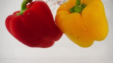 Kırmızı ve sarı biber düşüyor suya su sıçramalarına ve kabarcıklar, ağır çekim yakın çekim ile