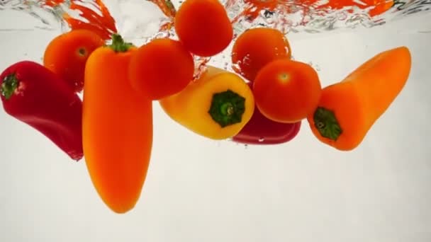 Зроблена страва свіжі овочі, перець і помідори вишні падають у воду, повільний рух крупним планом — стокове відео