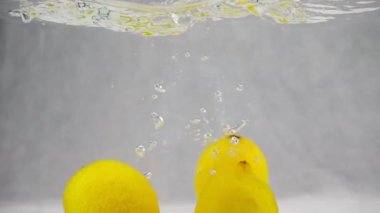 Üç sarı limon su kabarcıkları ile aynı anda girer. Ağır çekim video.