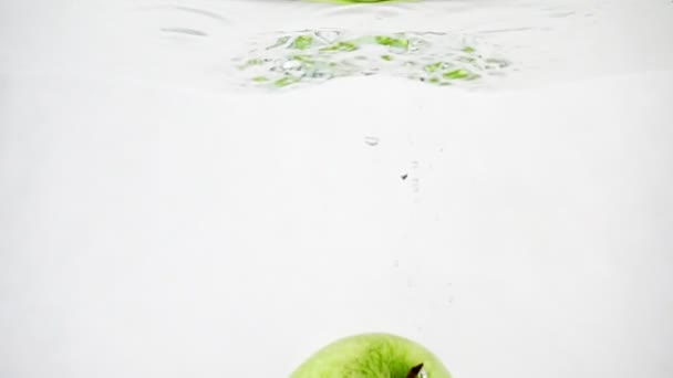 Fällt der grüne Apfel ins Wasser. isolierter Apfel auf weißem Hintergrund in Zeitlupe. — Stockvideo