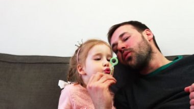 Mutlu bir baba ve onun sevimli çocuk darbeler birlikte yanardöner bir sabun baloncuklar ağır çekimde.