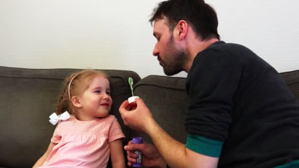 Ένας πατέρας φυσάει μια σαπουνόφουσκα δεξιά επάνω σε μύτη του κόρες σε αργή κίνηση. Τα γέλια μωρών. — Αρχείο Βίντεο