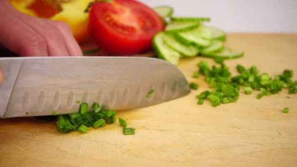Cortar cebollas verdes con un cuchillo en una tabla de madera, cámara lenta — Vídeo de stock