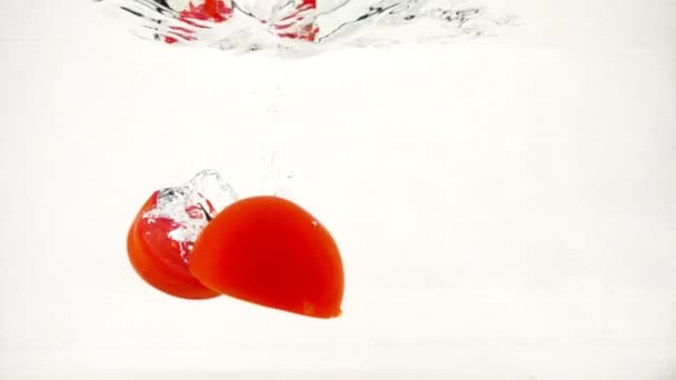 Juicy tomatoes halves are immersed in water with splashes and bubbles, slow motion close-up — Stock Video